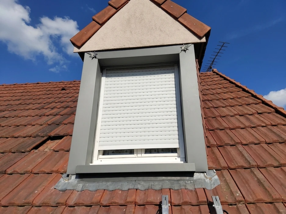 Lucarne de toit avec volet roulant blanc entièrement déployé, encadrée d'un dormant PVC gris anthracite