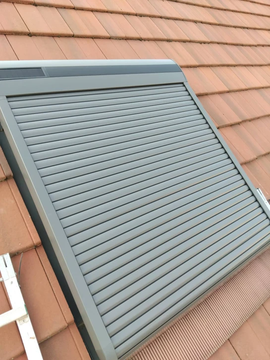 Volet roulant extérieur en aluminium anodisé gris anthracite, installé sur une fenêtre de toit en pente