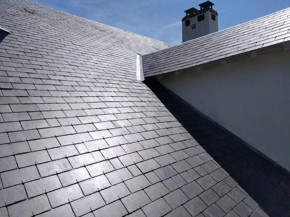 Toiture rénovée en ardoise naturelle grise, à faible pente, avec quatre fenêtres de toit type Velux intégrées