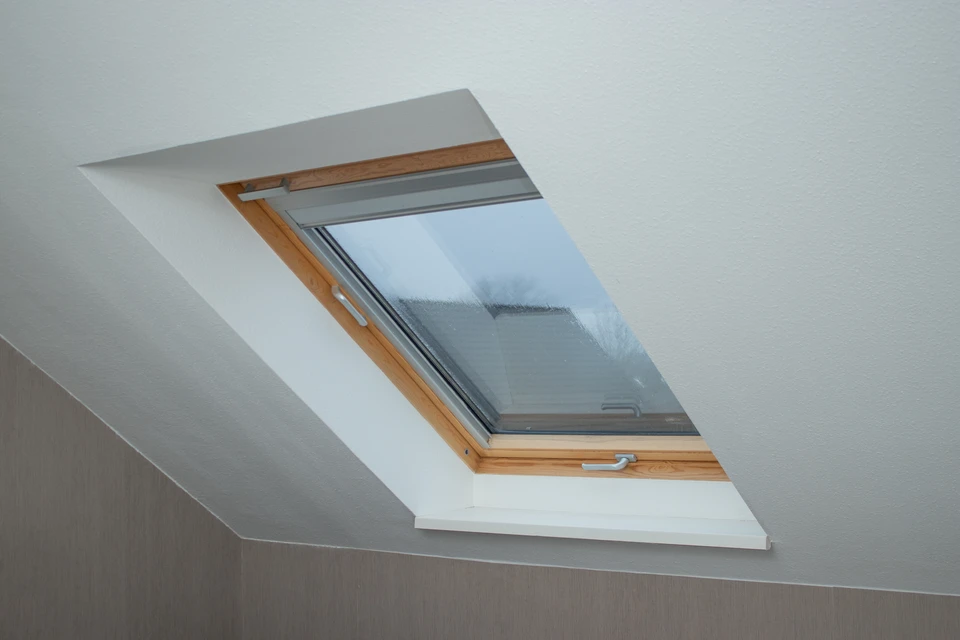 Lucarne de toit en ardoise avec volet roulant blanc sur cadre PVC gris anthracite, vue en plongée depuis le toit en tuiles terre cuite